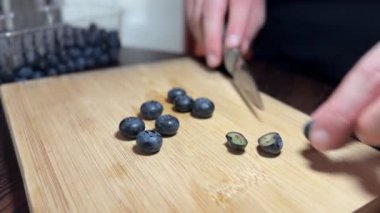 Bir insan ahşap kesme tahtasıyla farklı boyutlarda taze yaban mersini keser. Böğürtlenli bir konteynır yakınlarda duruyor. Yaz meyvesi, sağlıklı ve mevsimlik atıştırmalıklar.