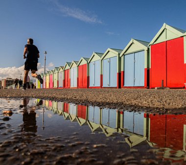 Akşamüstü Brighton Sahil Önü boyunca Yansıyan Sahil Kulübeleriyle Koşu