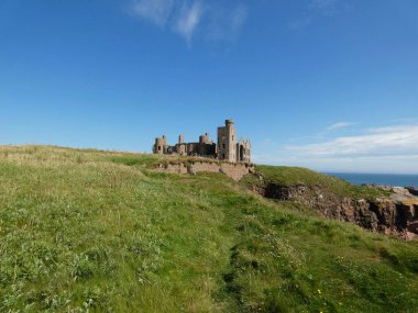 Slains Kalesi, İskoçya 'nın kuzeydoğu kıyısındaki engebeli deniz kayalıklarının tepesine çarpıcı bir şekilde tünemişti. Tarihi şatonun yıpranmış taş duvarları, yemyeşil otlar ve vahşi kıyı bitkileriyle çevrili derin mavi Kuzey Denizi 'ne tepeden bakar.