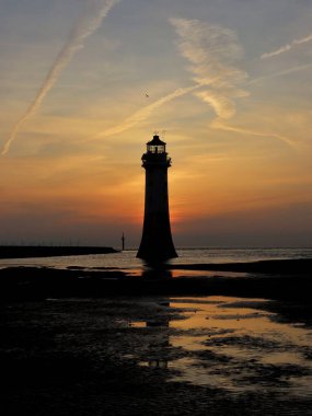 İkonik New Brighton Deniz Feneri zarif zıtlıklarla çizilmiş canlı bir günbatımı gökyüzüne karşı cesur bir siluet gibi duruyor. Günün son ışığı, deniz fenerinin yapısını aydınlatan sıcak bir parıltı saçar..