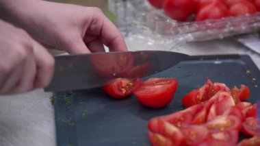 Kesme tahtasındaki olgun kırmızı domatesleri mutfak bıçağıyla dikkatlice dilimleyen kadın ellerine yakın plan. Taze ve doğal yemek hazırlama sahnesi. 