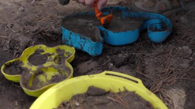 Kum ve Çamurdaki sarı oyuncak vinç ve diğer renkli oyuncaklarla etkileşime giren bir çocuğun yakın çekimi. Yaratıcı oyun zamanı boyunca neşeli ve yaratıcı bir an..