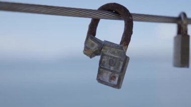 Broken Padlock Hanging on Steel Cable Against Blue horisont. Concept of vulnerability, lost security, or passage of time.
