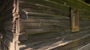 Sıcak güneş ışığıyla aydınlatılan küçük pencereli eski ahşap bir ev. Klasik kırsal dokular, odunların doğal yaşlanması ve huzurlu ışıklandırma, kırsal kesimde nostaljik bir havayı çağrıştırıyor..