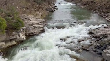 İlkbaharın başlarında kayalık arazide akan bir dağ nehrinin geniş manzarası. Sahne, taşların üzerine düşen beyaz suyla hızlı hareket eden şelalenin yakın çekimine sorunsuzca geçiş yapacak. Doğanın gücü.