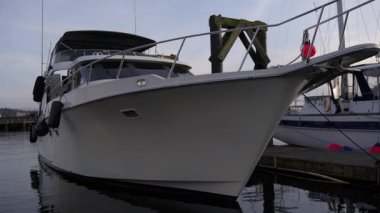 Sakin bir akşam ışığında sessiz bir marinada demirli büyük beyaz bir yatın yakın çekimi. Yansımalar suda hafifçe dalgalanır, deniz yaşam tarzını ve deniz zarafetini gösterir..