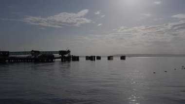 Gün doğumunda iskelesi olan sakin bir deniz manzarası. Yumuşak su, yumuşak ışık, sabahın erken saatlerinde atmosfer.