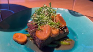 Mavi seramik tabakta taze yeşillik ve havuçlu leziz ızgara biftek. Üst manzara, canlı renkler, restoran tarzı servis, iştah açıcı yemekler..