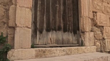 Taş çerçeveli eski bir ahşap kapının alçak açılı görüntüsü. Kamera basamaklardan yukarıya doğru hareket ederek antik mimariyi ve gökyüzünü ortaya çıkarıyor. Sinema sahnesi tarihi, gizemi ve zamansız atmosferi çağrıştırıyor.