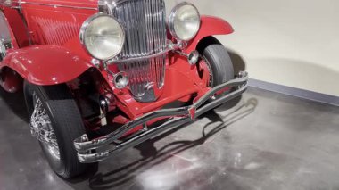 Krom ızgaralı, büyük yuvarlak farlı ve parlak tamponlu kırmızı klasik bir arabanın ön ucu..