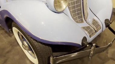 Kavisli kapüşonlu antika araba, krom radyatör ızgarası ve çift yuvarlak farlar.