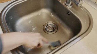 Süngerli bir el, metal bir mutfak lavabosunu temizler. Günlük temizlik, ev bakımı, temizlik konsepti.. 