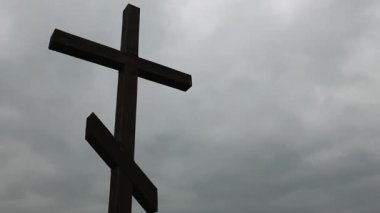 Gri bulutlu gökyüzüne karşı iki kavisli ahşap Ortodoks haçı.