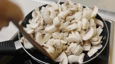 Tahta bir spatulayla karıştırılmış doğranmış mantarlı tavanın üst görüntüsü. Yemek pişirme, yemek tarifleri ve sebze hazırlama temaları için mükemmel..