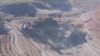 İnsansız hava aracı tarafından yakalanan devasa bir açık maden ocağının hava görüntüleri. Teraslı kaya katmanları ve madencilik ekipmanları görülebilir. Çekim, kuru bir arazide ölçek, erozyon ve sanayi faaliyetlerini gösteriyor..