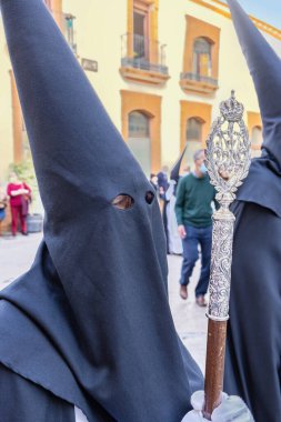 A Nazarene or penitent, holding a silver wand of command. 