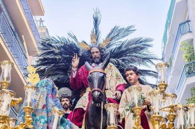 Christ riding a donkey in the Throne or platform of the Brotherhood of the La Borriquita, in procession by the narrow streets of the city clipart