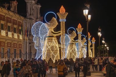 Seville, İspanya - 16 Aralık 2023: Seville, Endülüs 'teki San Telmo Sarayı' ndan meşale tutan bir melek şeklinde Noel ışıkları süslemesi. Hareket yüzünden insanlar bulanıklaşabilir.