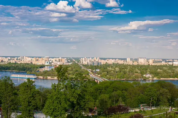 Kyiv 'in Dnipro Nehri' ni, manzaralı yeşilliği ve canlı mavi gökyüzünün altında hareketli şehir mimarisini sergilerken muhteşem bir panoramik görüntüsü..