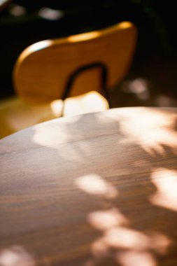 Kapalı alanda doğanın sanatı. Sıcak noktalı güneş ışığı ve yaprak gölgelerinin soyut görüntüsü pürüzsüz bir tahta masa yüzeyinde karmaşık desenler yaratıyor. Doku ve doğal ışığı vurgular.