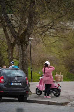 Tallinn, Estonya - 19 Nisan 2025: Tallinn Old Town 'da scooter' a hazırlanan kadın. Aynı renkte pastel scooter 'ın yanında pembeye bürünmüş, hasır sepetli..