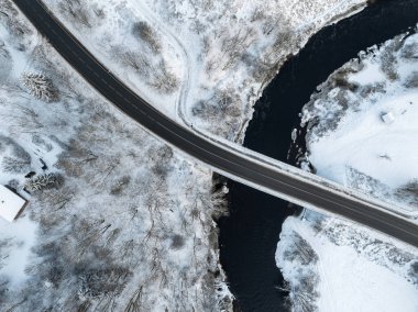 Estonya 'nın Tallinn kentindeki Pirita Nehri' nin kışın havadan görünüşü. Karla kaplı bir manzara, kıvrımlı nehri geçen parlak siyah bir yol köprüsü.