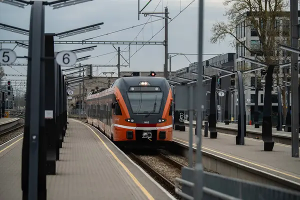 Tallinn, Estonya - 19 Nisan 2025: Bulutlu bir bahar gününde Baltık İstasyonu 'nda (Estonya - Balti Jaam) modern turuncu tren. Şehir demiryolu taşımacılığı çağdaş mimariyle karşılaşıyor.
