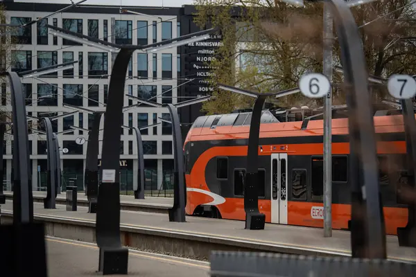 Tallinn, Estonya - 19 Nisan 2025: Modern Elron treni Baltık İstasyonu 'nda (Estonya - Balti Jaam). Gösterişli tasarım, turuncu-siyah renkler ve şehir arkaplanı verimli toplu taşımayı yansıtıyor.