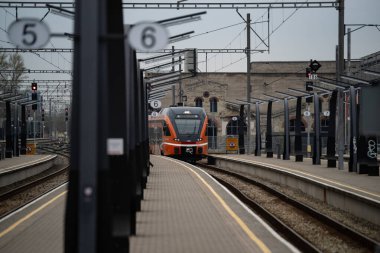 Tallinn, Estonya - 19 Nisan 2025: Bulutlu bir bahar gününde Baltık İstasyonu 'nda (Estonya - Balti Jaam) modern turuncu tren. Şehir demiryolu taşımacılığı çağdaş mimariyle karşılaşıyor.