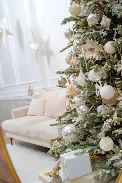 Beyaz, gümüş ve altın Noel ağacının gölgeleriyle süslenmiş zarif süsler büyük, süslü bir aynaya yansıyor. Arka planda beyaz ve bej renkli zarif iç mekan.