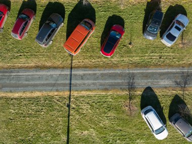 Paide, Estonya - 7 Mart 2025: Dar bir yolun yakınındaki çimlere parkedilmiş arabaların yukarıdan aşağı havadan görünüşü, güneşli bir günde gölgeler. Simetrik düzen, canlı araç renkleri ve doğal dokular.