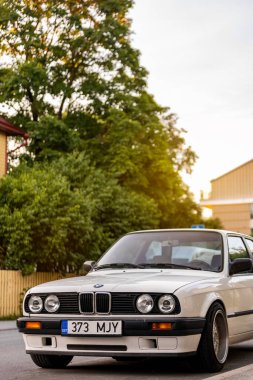 Tallinn, Estonya - 9 Temmuz 2025: Klasik beyaz BMW 3 serisi E30, 1991 model, altın saat boyunca Kalamaja bölgesinde sakin bir yerleşim yerine park edilmiş..