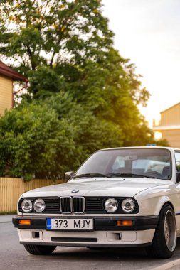 Tallinn, Estonya - 9 Temmuz 2025: Klasik beyaz BMW 3 serisi E30, 1991 model, altın saat boyunca Kalamaja bölgesinde sakin bir yerleşim yerine park edilmiş..
