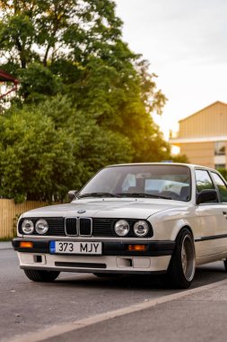 Tallinn, Estonya - 9 Temmuz 2025: Klasik beyaz BMW 3 serisi E30, 1991 model, altın saat boyunca Kalamaja bölgesinde sakin bir yerleşim yerine park edilmiş..