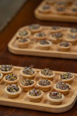 Tahta tepsilerde servis edilen mini mantarlı turtalar. Mikroyeşilliklerle kaplı lezzetli vejetaryen aperatifler, yemek servisi, partiler veya gurme büfe sunumları için mükemmel.