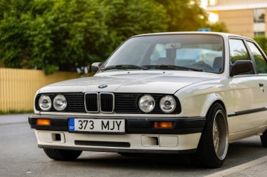 Tallinn, Estonya - 9 Temmuz 2025: Klasik beyaz BMW 3 serisi E30, 1991 model, altın saat boyunca Kalamaja bölgesinde sakin bir yerleşim yerine park edilmiş..