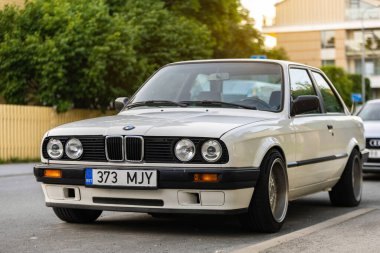 Tallinn, Estonya - 9 Temmuz 2025: Klasik beyaz BMW 3 serisi E30, 1991 model, altın saat boyunca Kalamaja bölgesinde sakin bir yerleşim yerine park edilmiş..