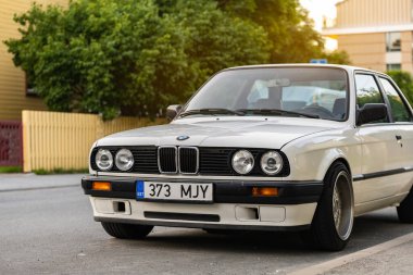 Tallinn, Estonya - 9 Temmuz 2025: Klasik beyaz BMW 3 serisi E30, 1991 model, altın saat boyunca Kalamaja bölgesinde sakin bir yerleşim yerine park edilmiş..