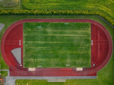 Estonya 'daki Vinni Stadyumu' nun havadan aşağı manzarası. Canlı kırmızı koşu yolu, yeşil bir futbol sahasının çevresini sarar. Etrafı tarlalarla çevrilidir..