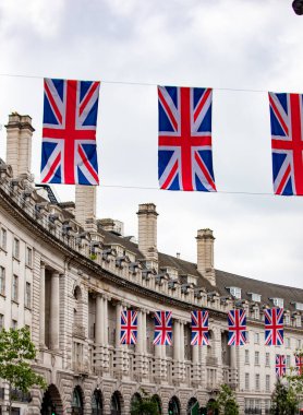 Union Jack bayrakları Londra 'da tarihi bir bina cephesini süslüyor. Bulutlu gökyüzü mimari detayları vurguluyor.