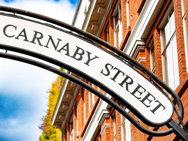 Londra 'daki ikonik Carnaby Sokağı tabelasına yakın plan, arka planda kırmızı tuğlalı bir bina..
