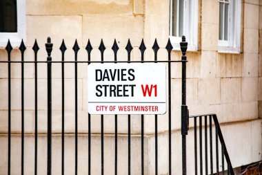 Westminster, Londra 'daki Davies Sokağı' nın sokak tabelası. Tabela siyah metal bir çitin üzerine asılmış ve arka planda bej bir bina var..