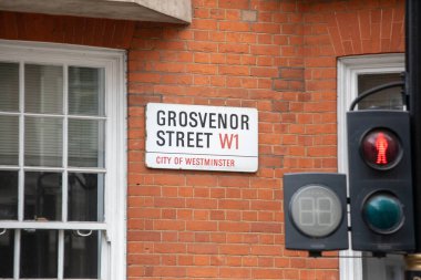 Westminster, Londra 'daki Grosvenor Caddesi' nin sokak tabelası. Trafik ışığı da var. Kırmızı tuğla duvar şehir sahnesine ekleniyor.