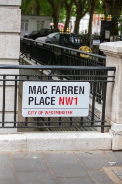 Londra 'nın Westminster şehrinde Mac Farren Place için bir sokak tabelası görüldü. Bölgede park halindeki arabalar ve klasik bir demir çit bulunuyor..
