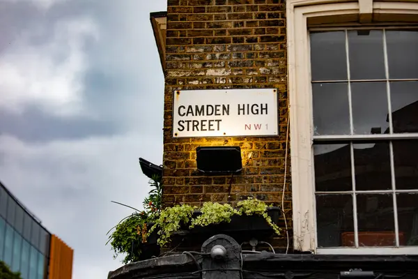 Londra 'daki Camden High Caddesi' ndeki sokak tabelasında NW1 posta kodu var. Tuğla bina ve bulutlu gökyüzü klasik bir şehir atmosferi yaratır..