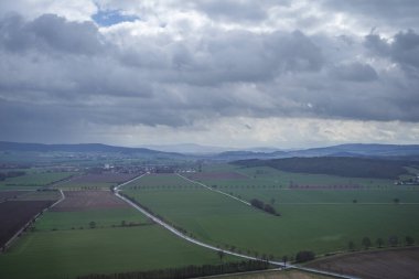 Kırsal alanların, yolların ve dramatik bulutlu gökyüzünün altında bir köyün panoramik manzarası.