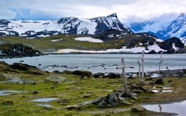 Bulutlu bir gökyüzünün altında dağlarla çevrili güzel bir göl görüntüsü.