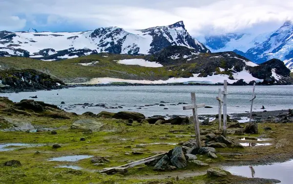 Bulutlu bir gökyüzünün altında dağlarla çevrili güzel bir göl görüntüsü.