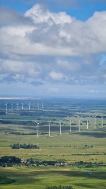 Rüzgar türbinlerinin geniş yeşil bir arazide döndüğü panoramik manzara teknoloji ve doğa arasındaki yenilenebilir enerji ve uyumu sembolize ediyor..