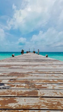 Yıpranmış ahşap bir iskele turkuaz bir denizin kristal berrak suları üzerinde uzanır. Gökyüzü parçalı bulutlu, sakin ve rahatlatıcı bir atmosfer yaratıyor..